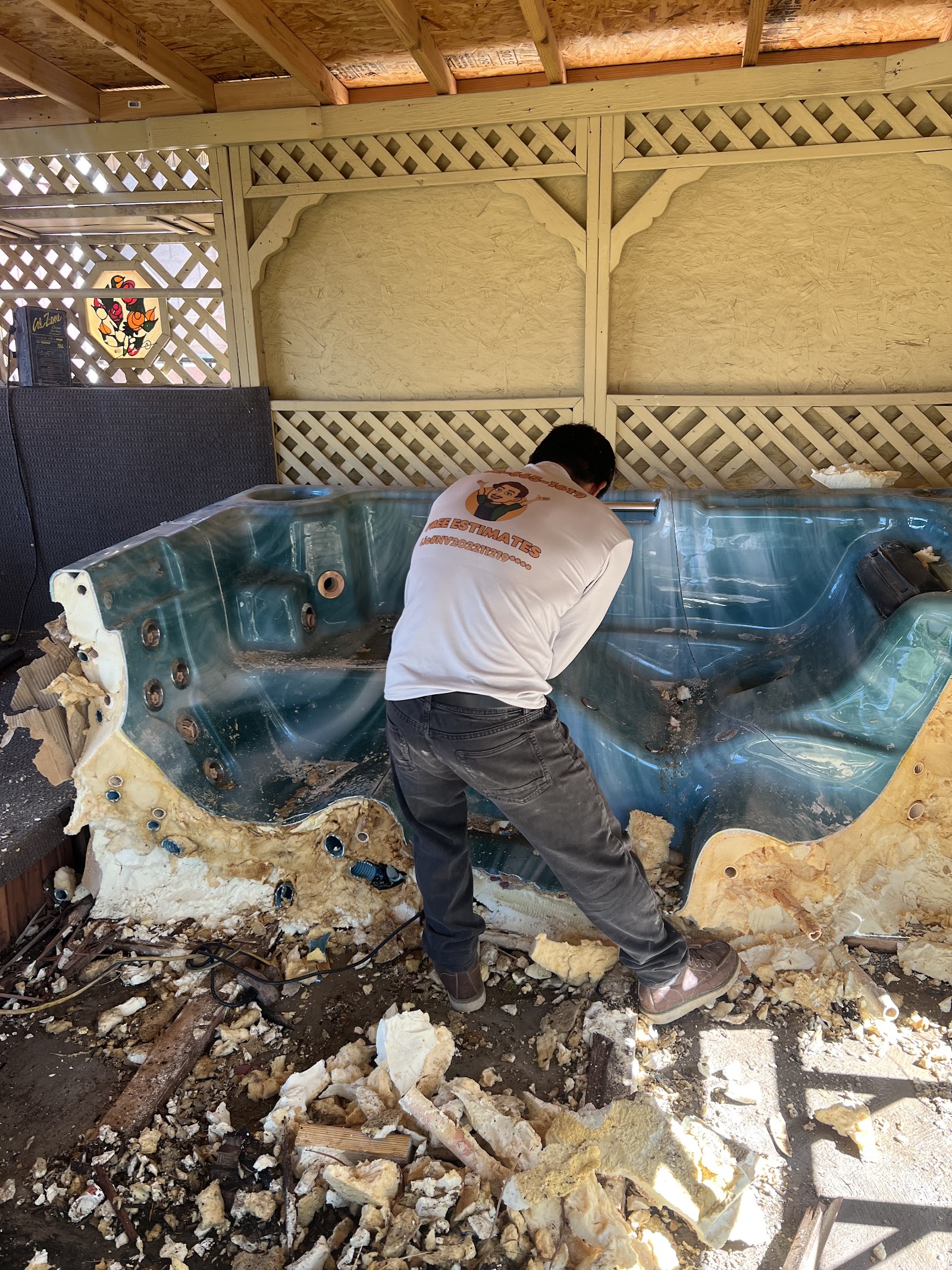 Worker in branded Eli's Junk Removal shirt demolishing an old hot tub under a patio