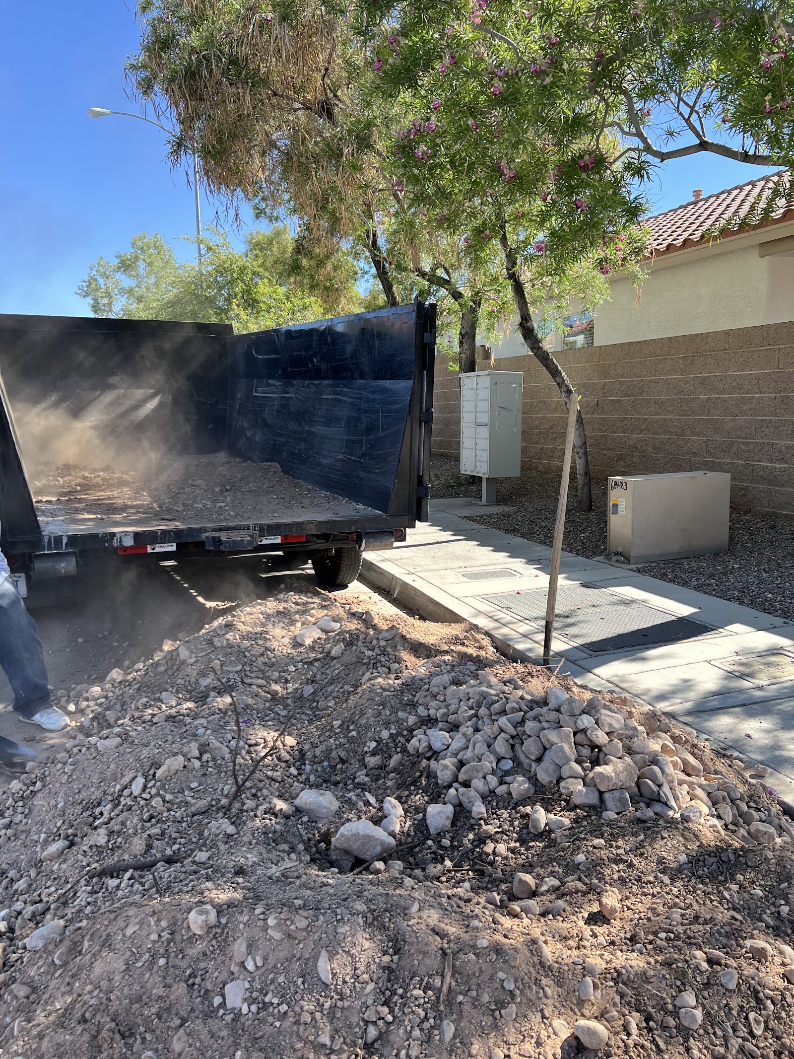 Dump trailer unloading rock and dirt debris near a residential sidewalk